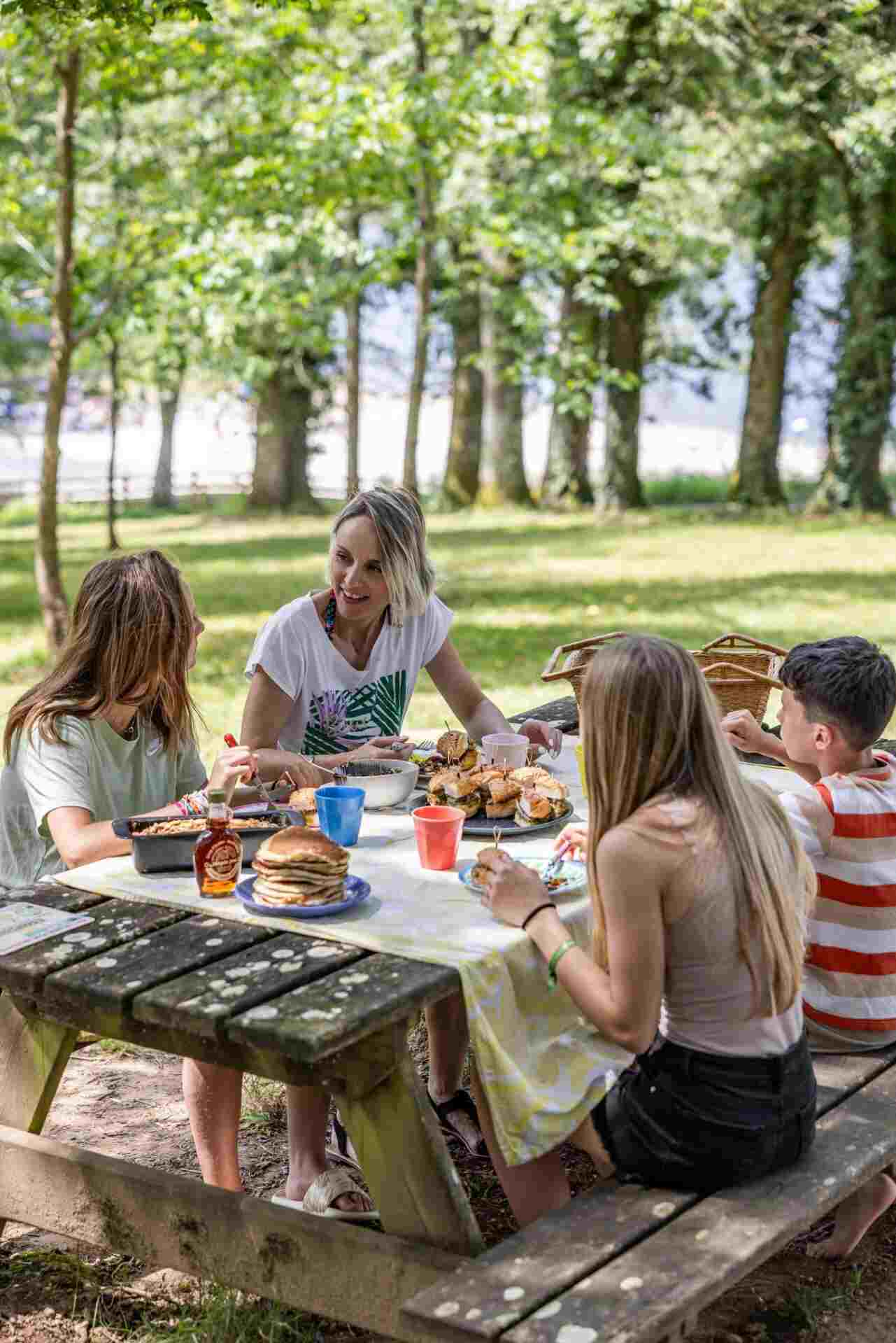A family with 3 teenagers eating at a picnic table in the middle of nature by Lake Rouffiac